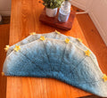 A light blue and white crochet blanket with yellow star appliques is folded in half on a wooden table.