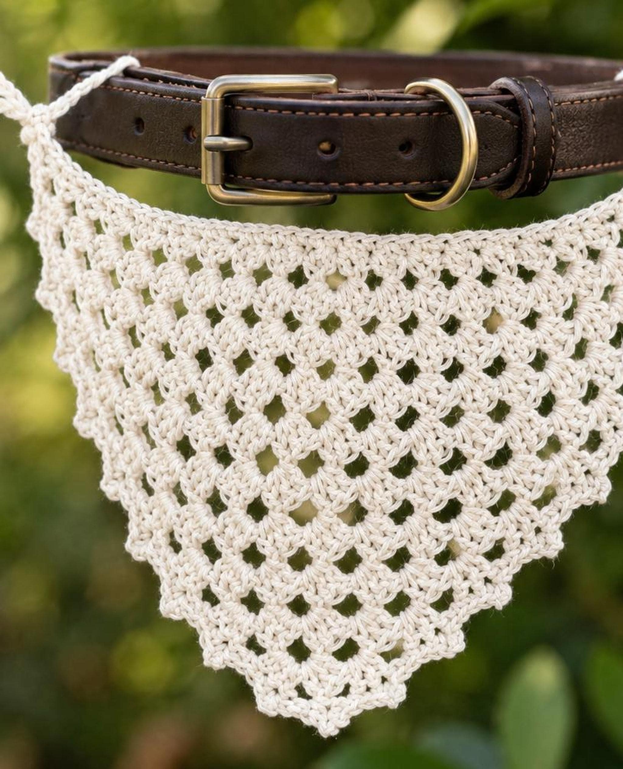 A close-up of a cream-colored, open-weave crocheted bandana, with a brown leather collar and buckle visible above it.