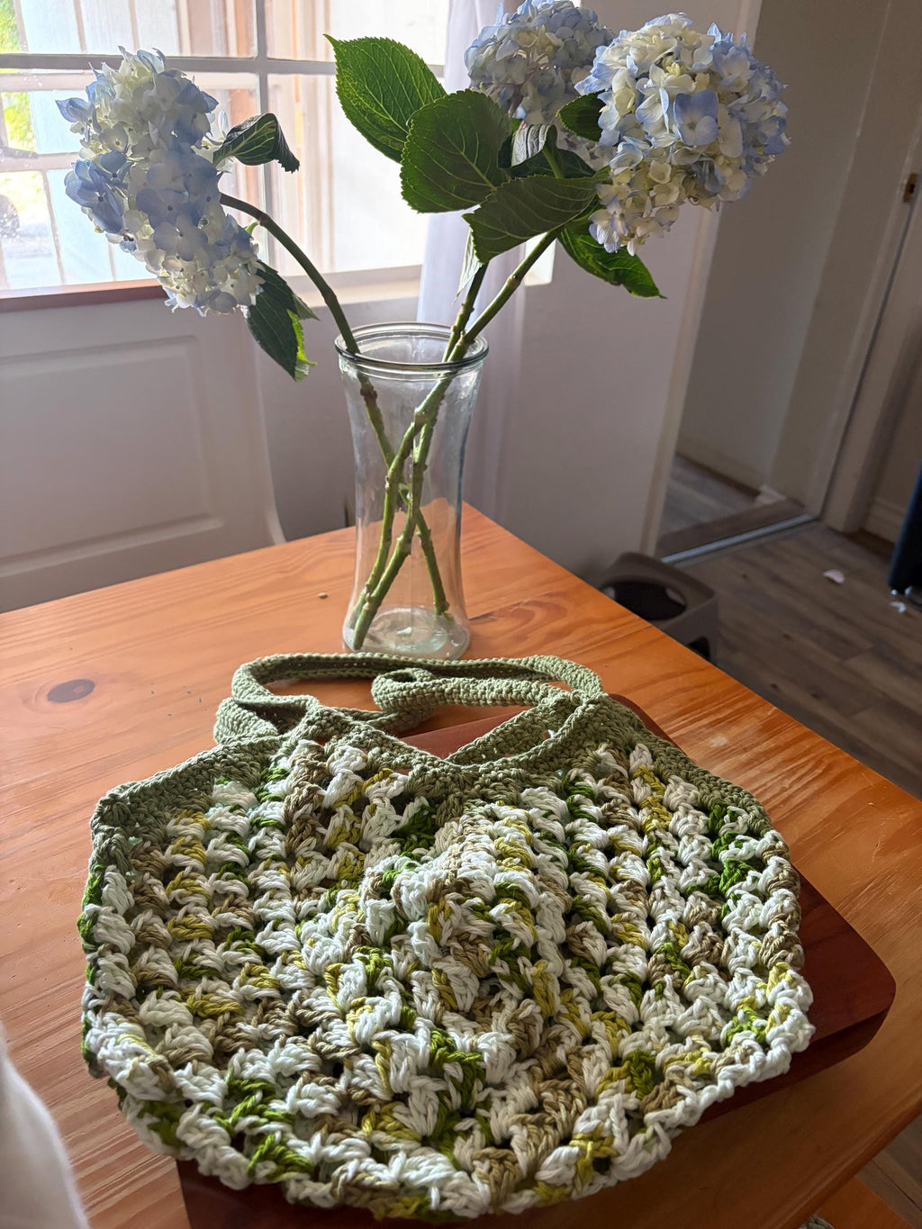 A green crochet market bag with white and light green accents is centered on a wooden table.