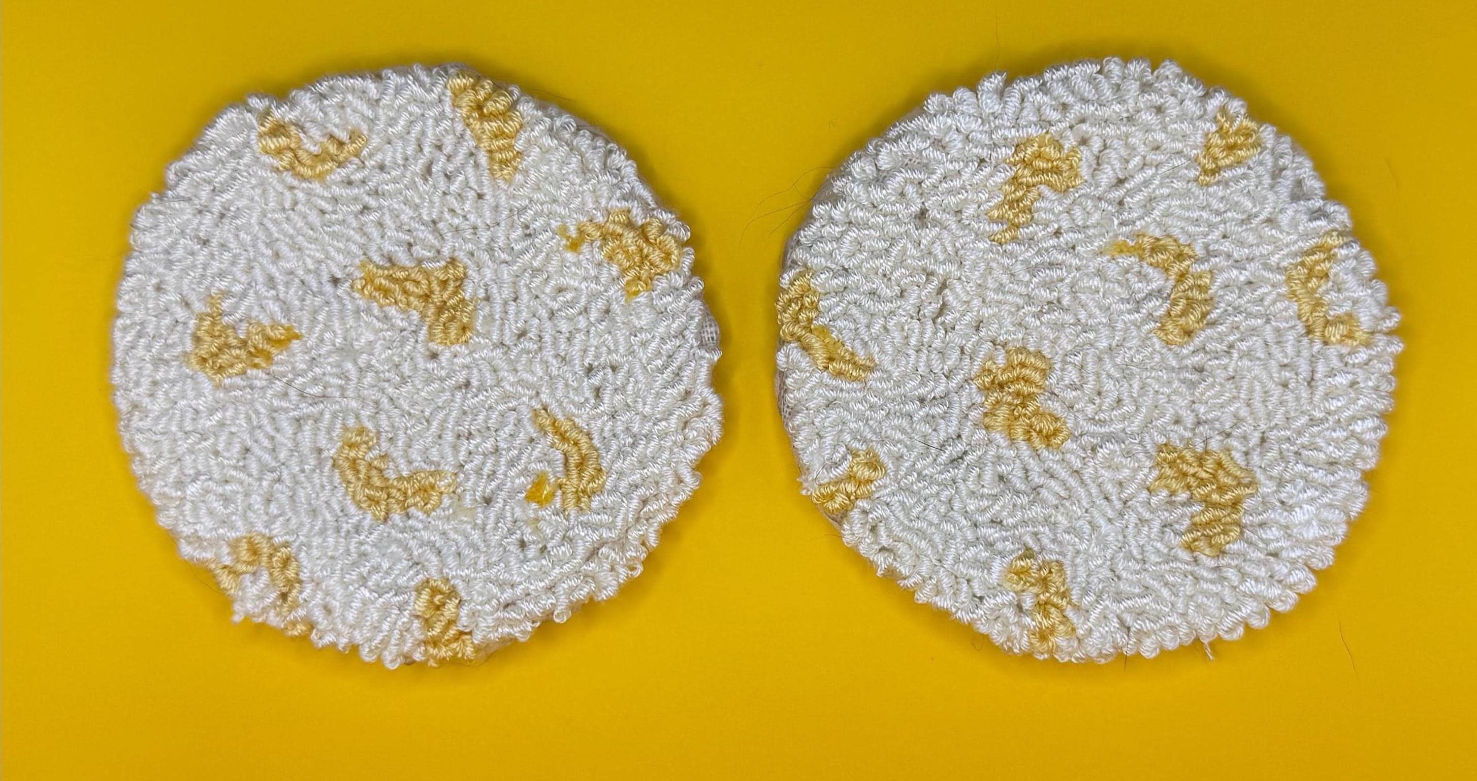 Two round punch needle coasters, each with a white base and scattered yellow accents, are displayed side-by-side on a yellow background.