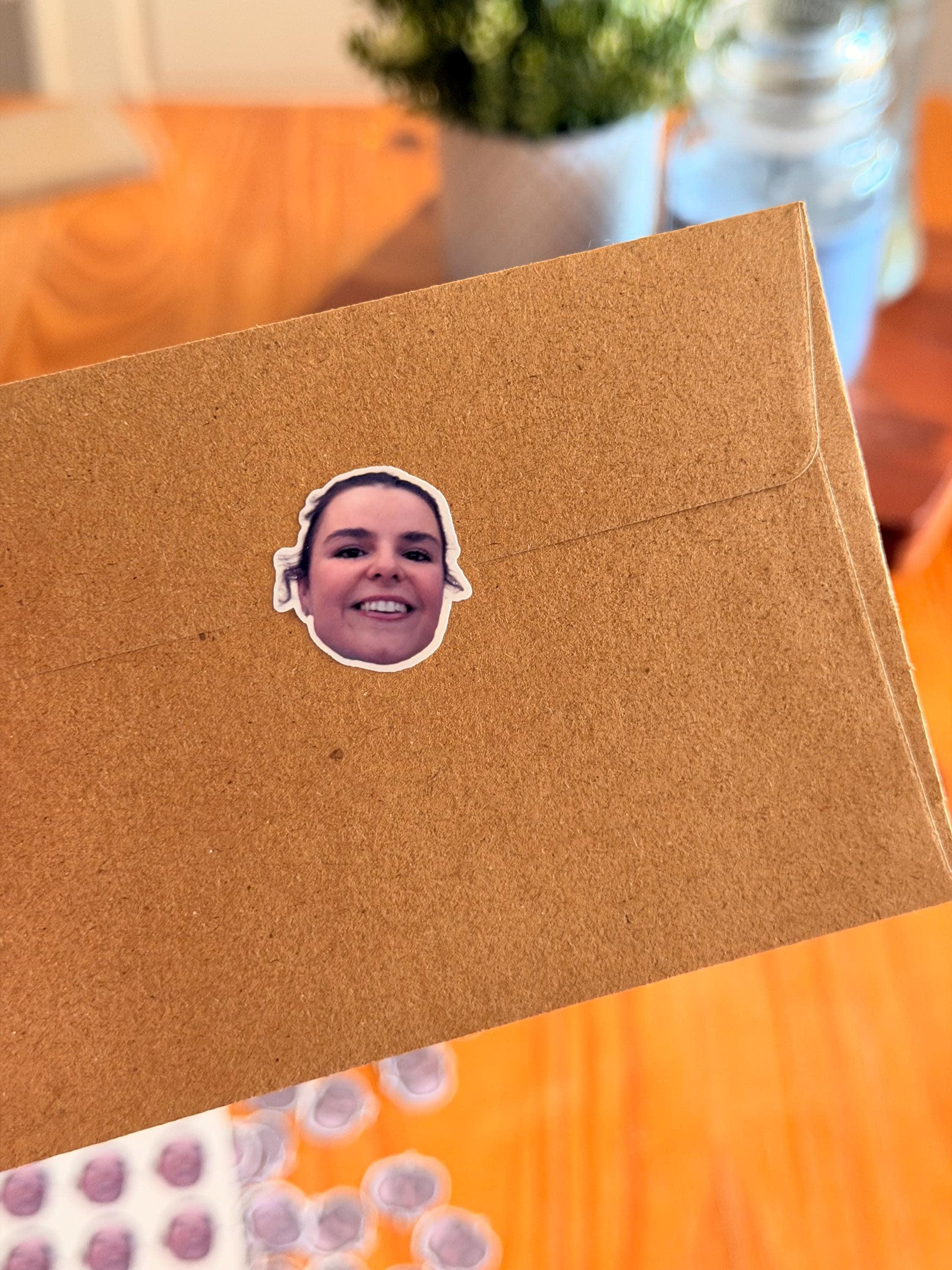 A close-up of a brown paper envelope sealed with a single round custom face sticker.