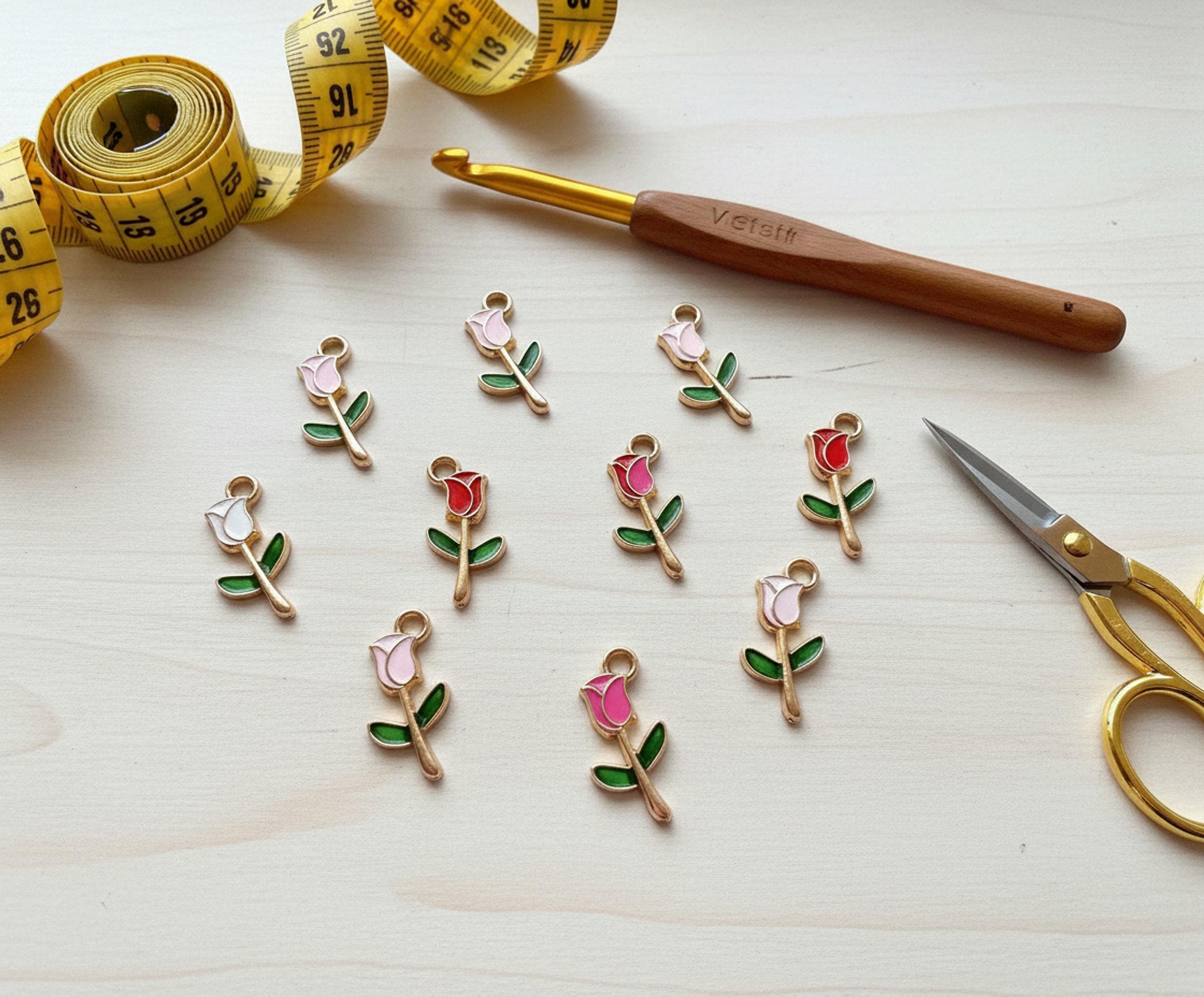 Flat lay of all 8 tulip stitch markers with crafting tools on a wooden surface.