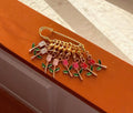 Eight enamel tulip stitch markers in shades of white, pink, and red, attached to a gold safety pin, resting on a brown surface.