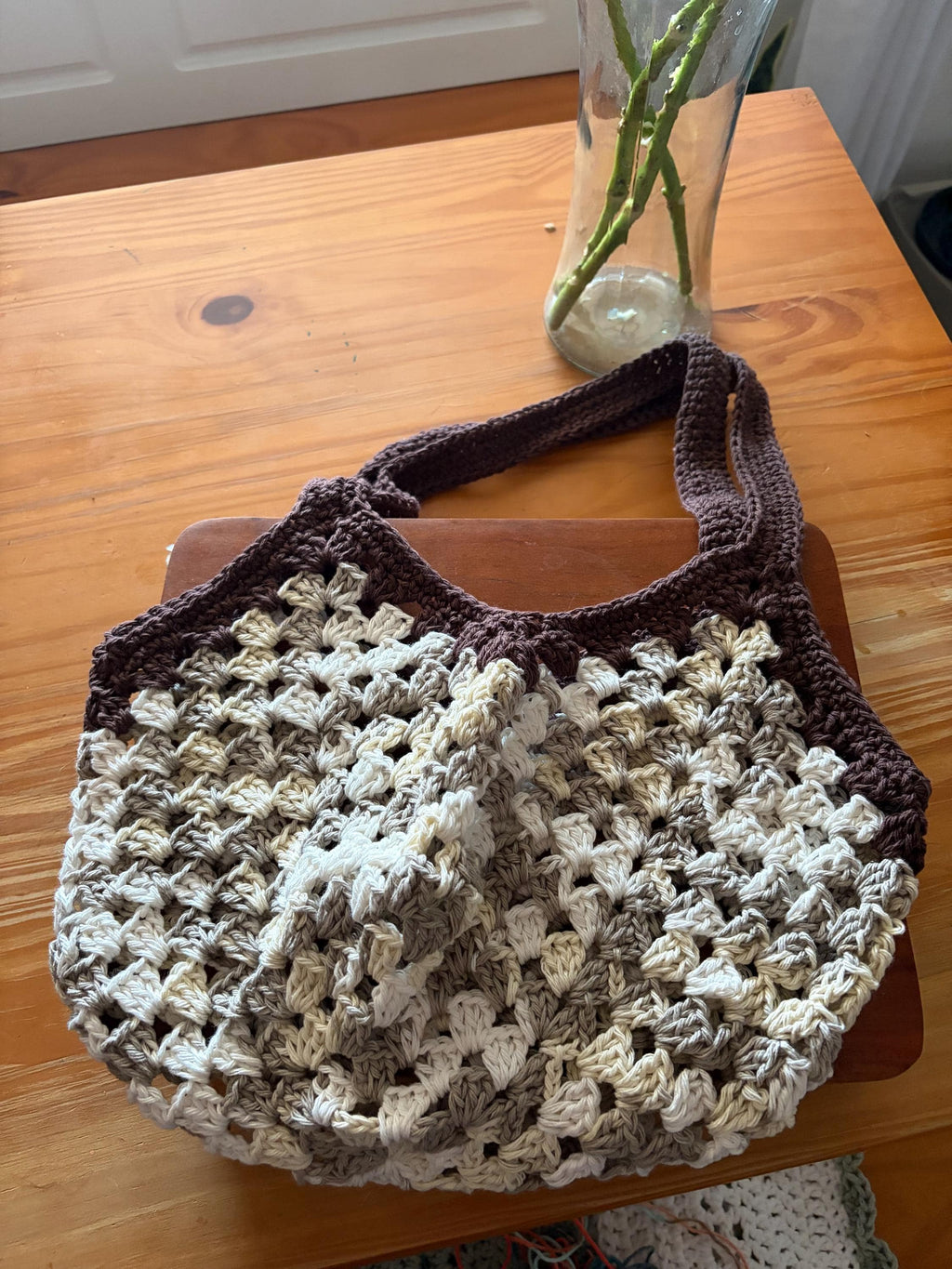 A brown crochet market bag with white and tan accents is centered on a wooden table.