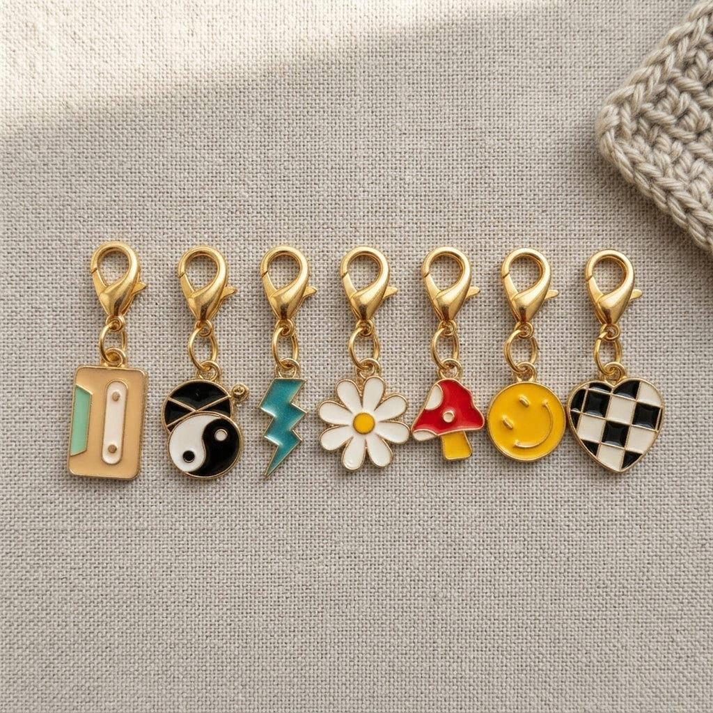 Close up of 8 enamel stitch markers with gold clasps on a linen surface.