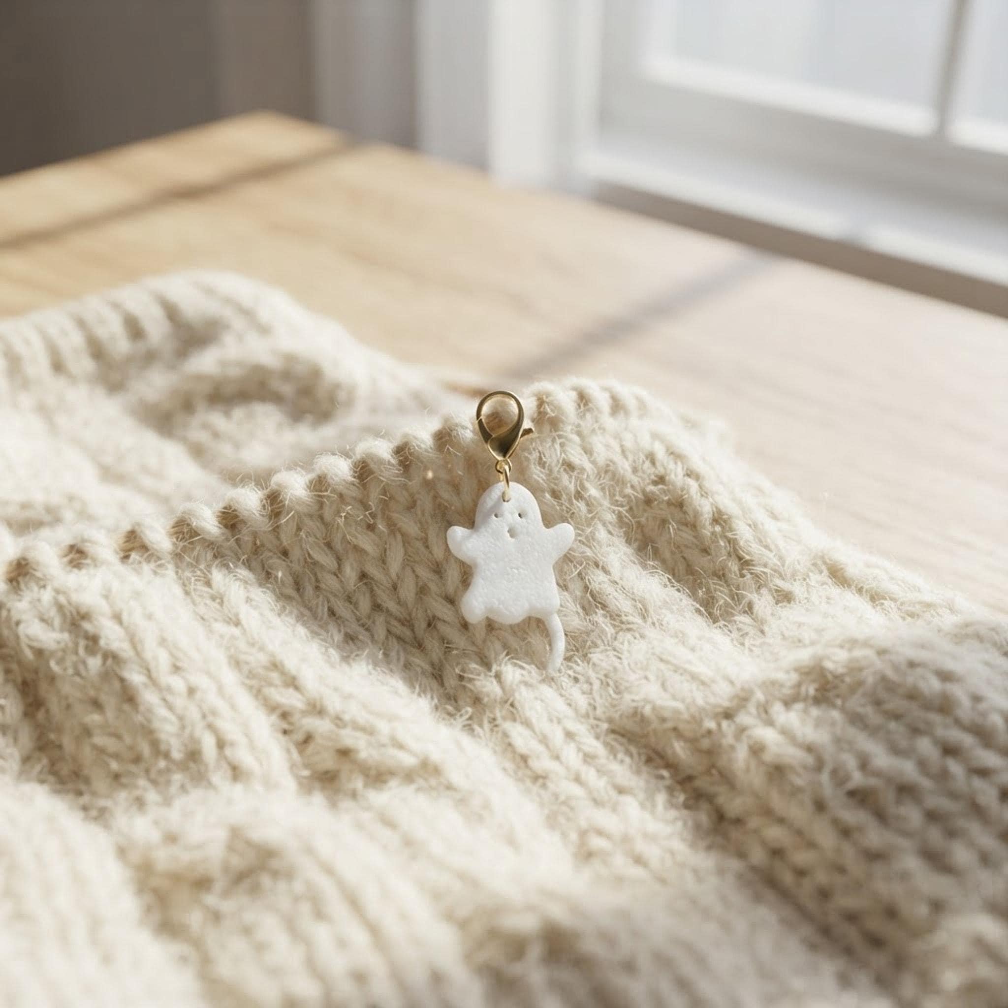 A white ghost stitch marker attached to a cream-colored knitted project on a wooden surface.