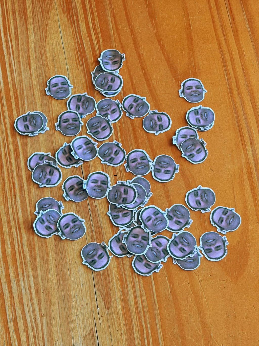 A collection of loose mini face confetti stickers scattered on a wooden table.