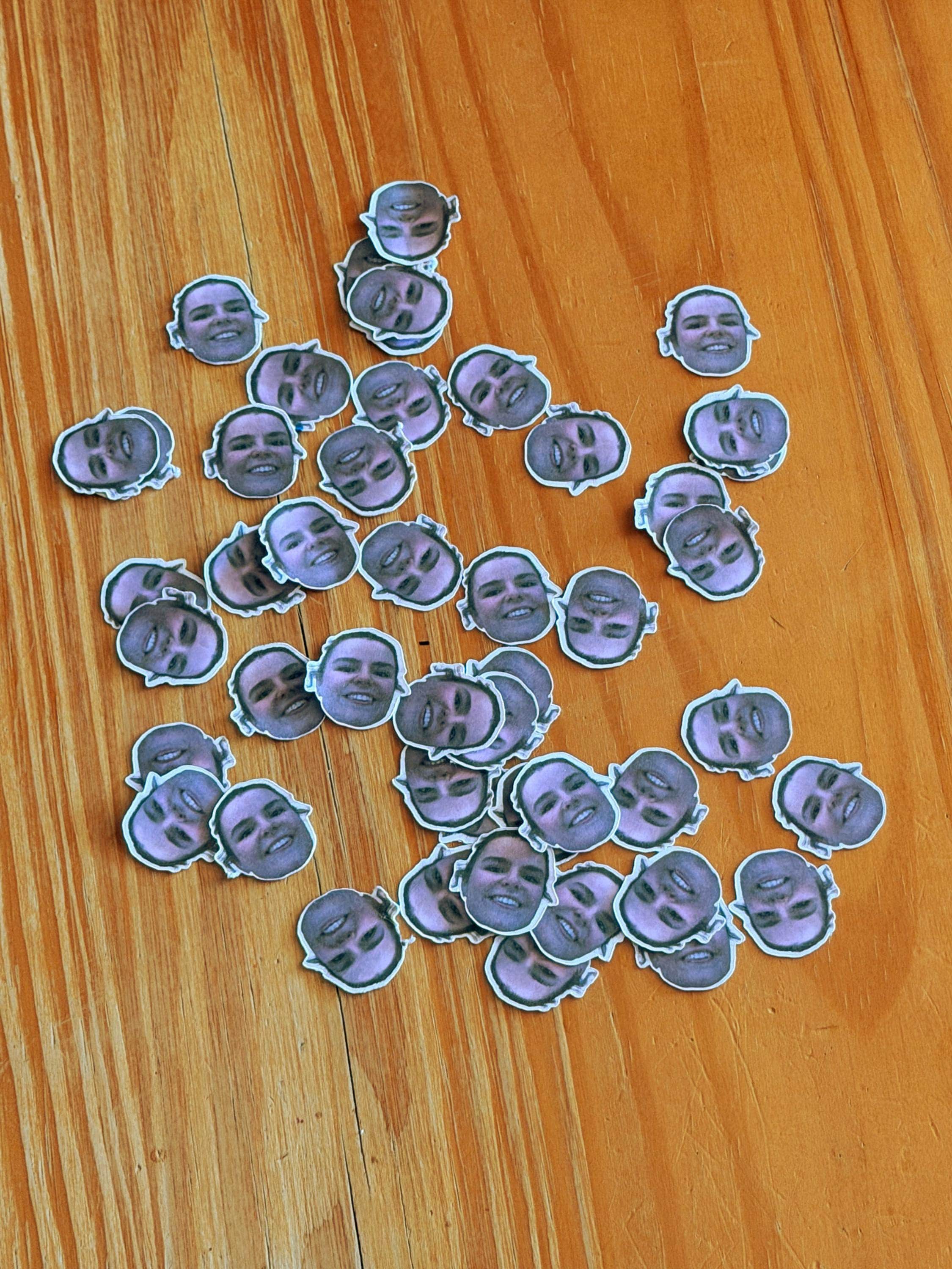 A collection of loose mini face confetti stickers scattered on a wooden table.