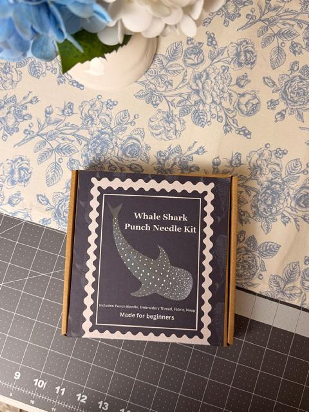 A cardboard box labeled Whale Shark Punch Needle Kit sits on a floral surface.