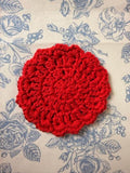 A single round red crochet coaster centered on a blue floral fabric background.