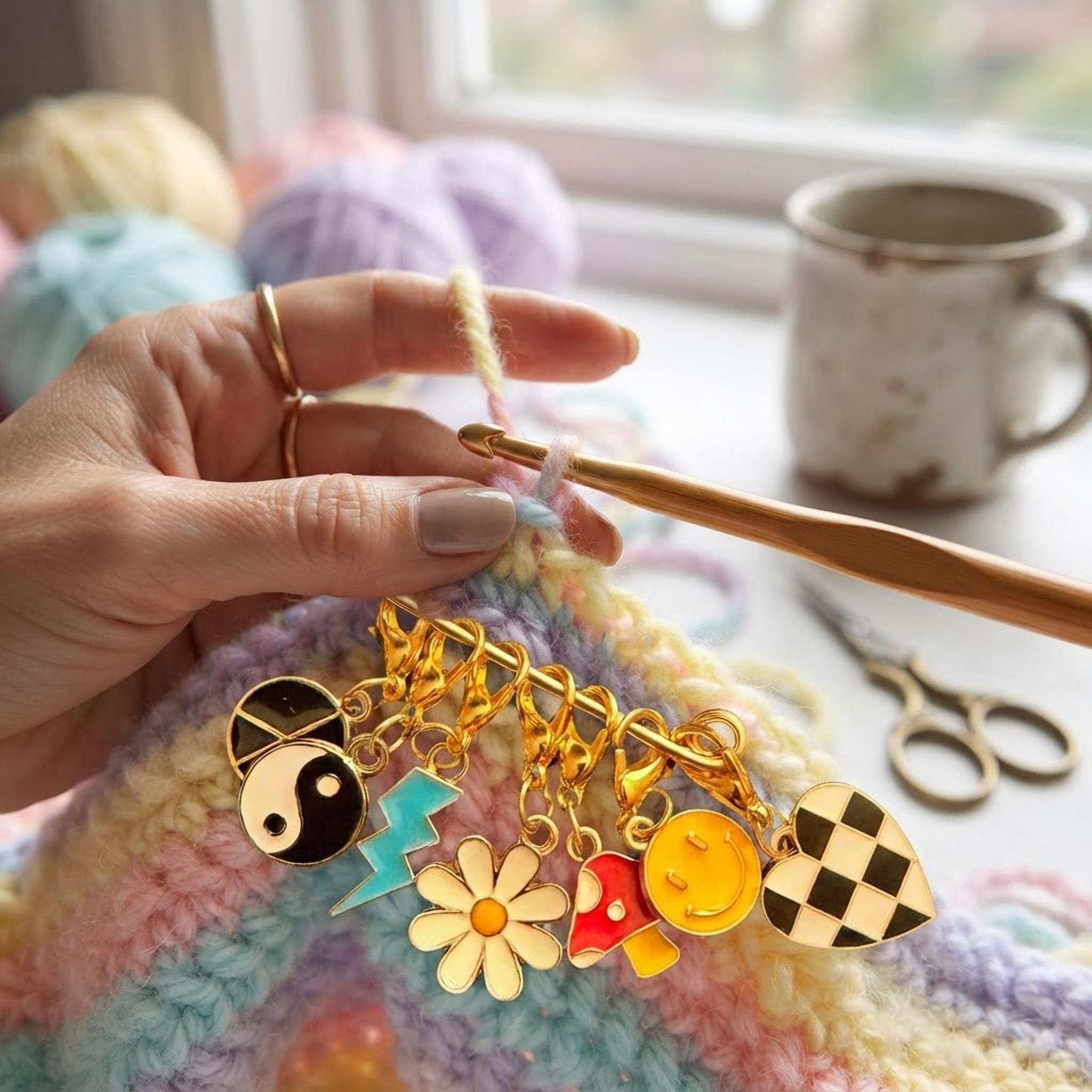 Hands crocheting with pastel yarn attached to Y2K enamel stitch markers featuring gold clasps.