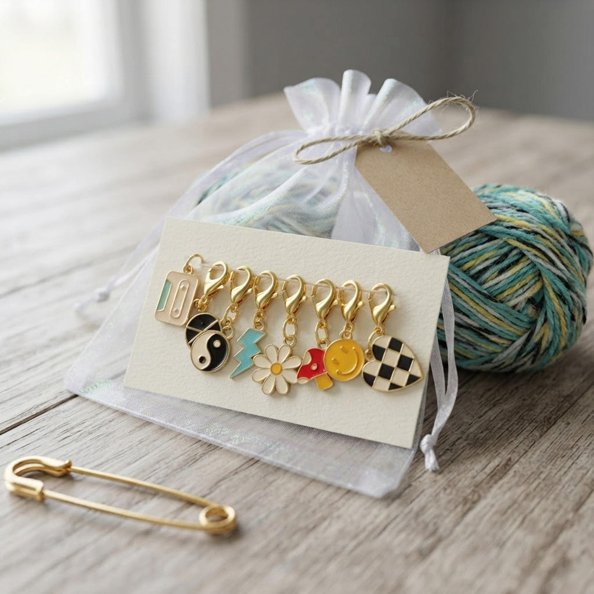 Set of 8 Y2K enamel stitch markers presented as a gift pouch next to yarn.