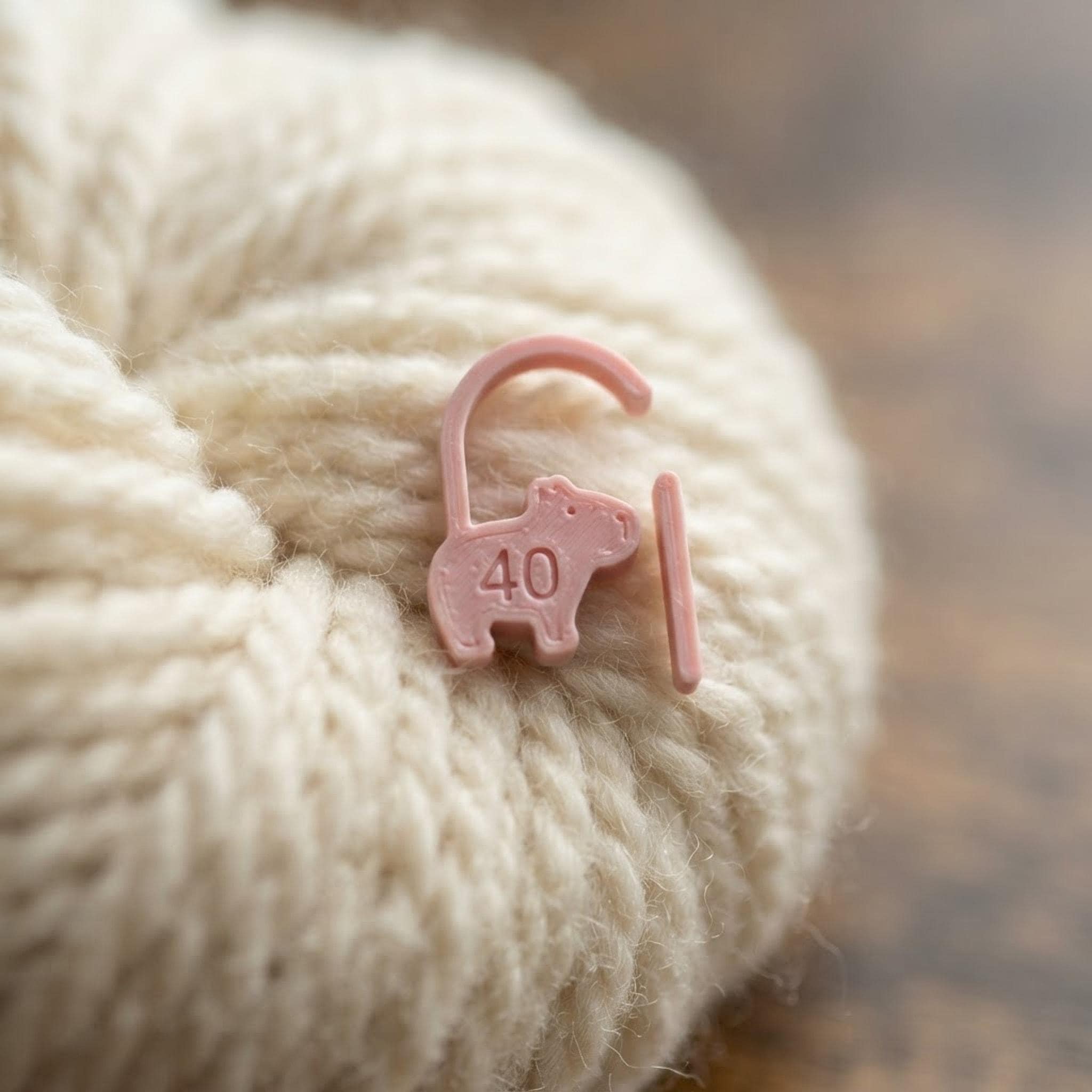 Macro close-up of a pink capybara stitch marker attached to textured cream yarn.