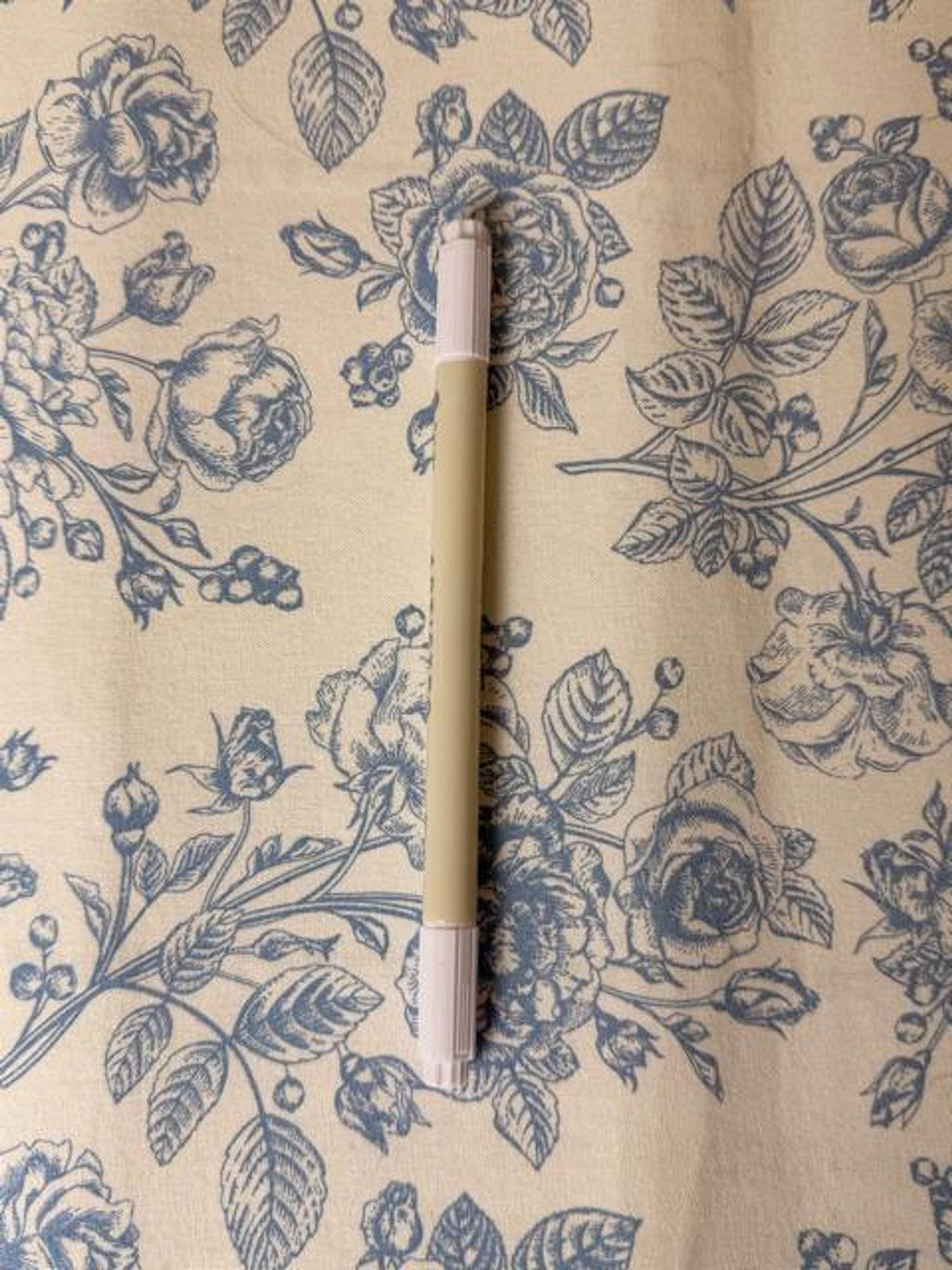 A beige and white marker pen rests vertically on a blue and white floral fabric.