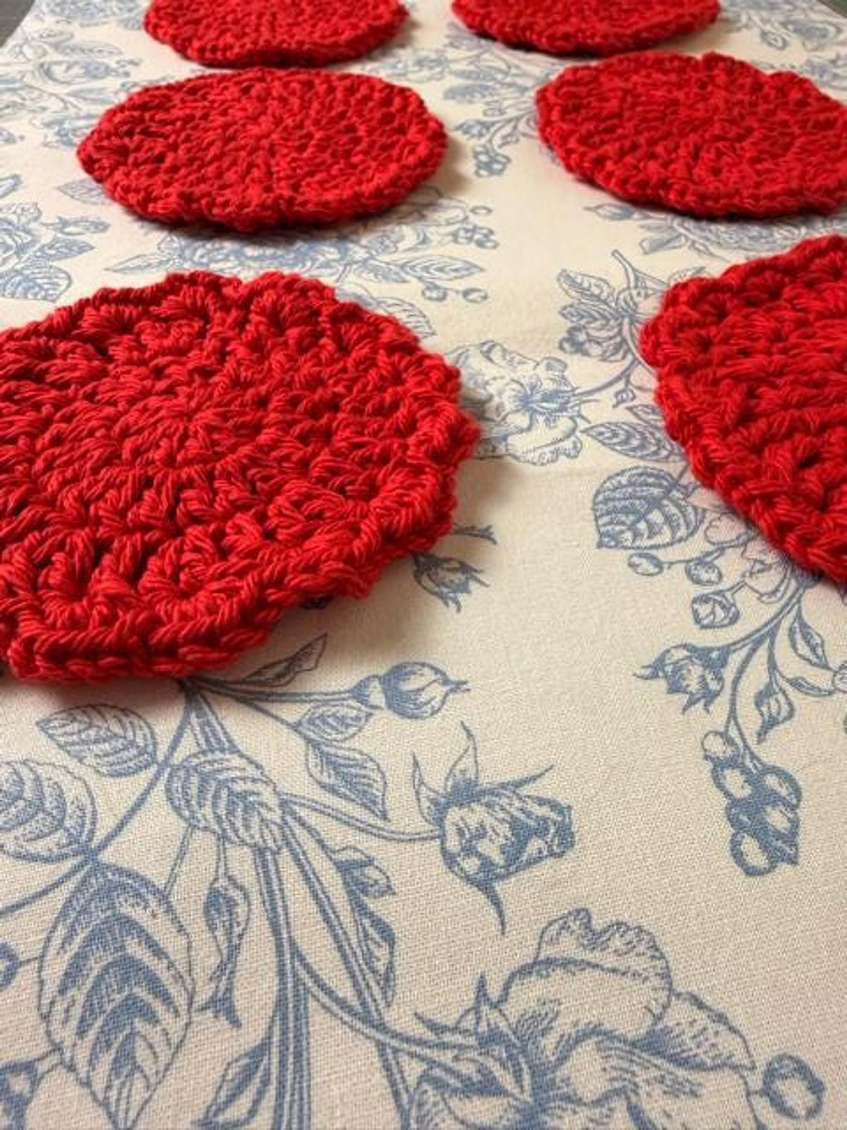 Several round red crochet coasters scattered diagonally across a blue floral tablecloth.